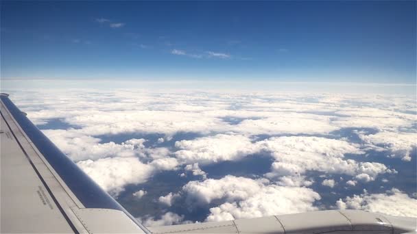 Tierra y nubes blancas bajo el ala de un avión durante el vuelo — Vídeo de stock