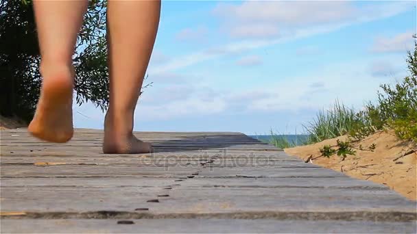 Босоногая девушка ходит по деревянному пирсу у моря — стоковое видео