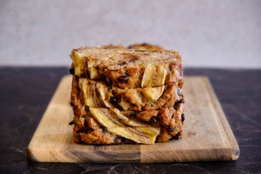 Tahta üzerinde servis edilen ev yapımı sağlıklı muz ekmeği, siyah mermer yüzey.