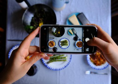Tagliatelle bolonez, kuşkonmaz ve salatayla akıllı telefon kullanarak yemek masasının fotoğrafını çekmek. Akıllı telefonlu yemek fotoğrafçılığı kavramı.