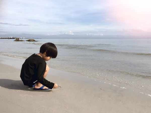 4 jaar oude Aziatische jongen zand schrijven op strand met zee en hemel ba — Stockfoto