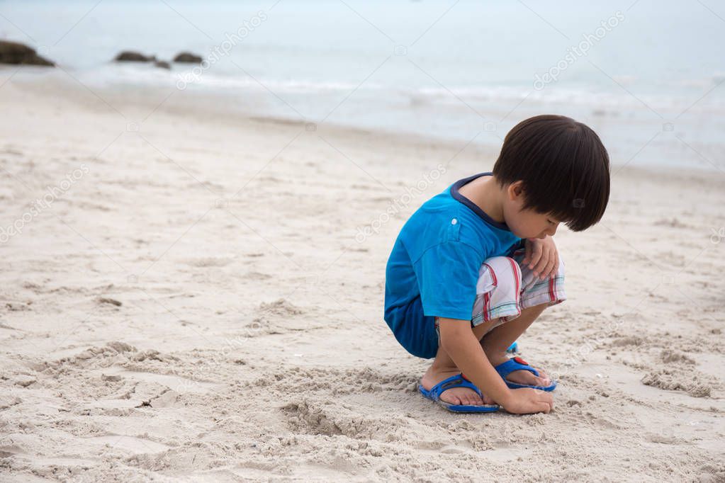 4 years old Asian boy sand writing lonely on beach with sea  bac