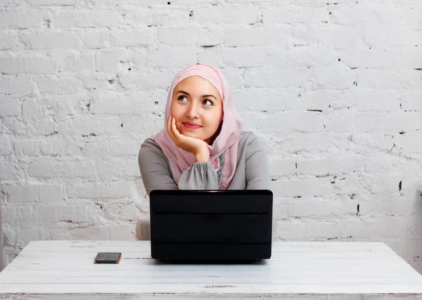 Мусульманская деловая леди, работающая за компьютером в офисе и думающая: Стоковая Картинка