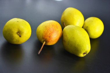 Siyah plastik arka planda parlak, lezzetli yeşil, kırmızı ve sarı armutlar bulunur. Düzgün beslenme, her gün için sağlıklı taze meyveler..