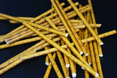 Undan yapılmış haşhaş tohumları olan lezzetli ve tatlı pipetler, siyah plastik bir arka plana saçılmış..