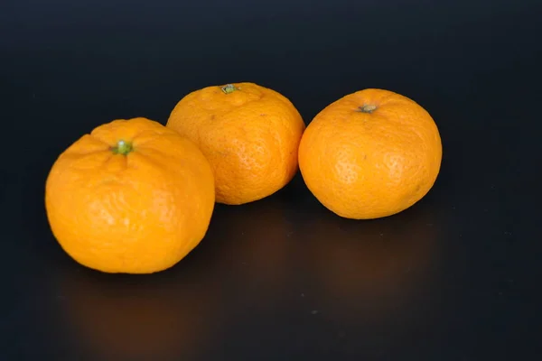 Saftige Früchte Drei Kleine Orangefarbene Mandarinen Liegen Auf Schwarzem Kunststoffhintergrund — Stockfoto