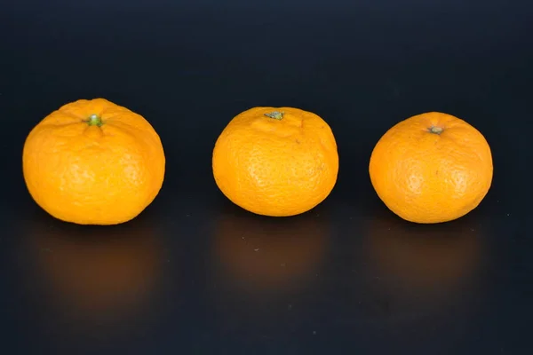 Soczyste Owoce Trzy Małe Pomarańczowe Mandarynki Leżą Czarnym Plastikowym Tle — Zdjęcie stockowe