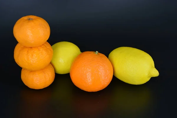新鮮な明るい果物 2つの黄色のレモン 3つの小さなオレンジみかん 1つの大きなミネラローラ黒いプラスチックの背景に位置しています おいしいと甘い果物 果物の花瓶 毎日のための健康的な食べ物 — ストック写真
