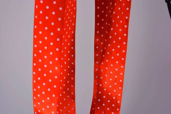 Red ribbon with white polka dots located on a white background. A wide colorful elegant wide ribbon curled in an interesting way.