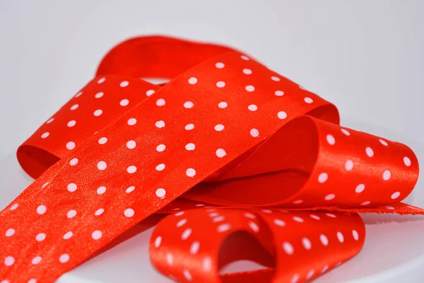 Red ribbon with white polka dots located on a white background. A wide colorful elegant wide ribbon curled in an interesting way.