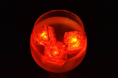 Lezzetli bir buzlu beyaz içeceğin içinde yüzen parlak kırmızı buz küpleri siyah buzlu bir zemin üzerinde konyak bardağında yer alır..