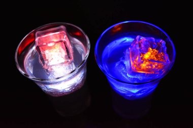 Beyaz bir içecek ile doldurulmuş dalları ve yaprakları olan şampanya bardağı siyah bir arka planda yer almaktadır. Farklı renklerde parlayan küçük buz küpleri bir bardakta süzülür, parti, kutlama.