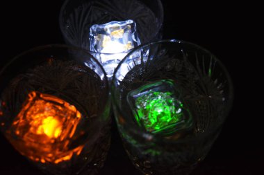 Kar taneleri şeklinde oymalı kristal şampanya bardakları siyah bir arka planda yer almaktadır. Parlak çokrenkli doidik parlayan buz küpleri suyun içinde yüzer..