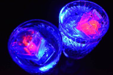 Kar taneleri şeklinde oymalı kristal şampanya bardakları siyah bir arka planda yer almaktadır. Parlak çokrenkli doidik parlayan buz küpleri suyun içinde yüzer..