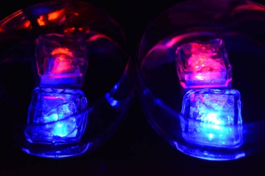 Siyah bir arka planda, farklı renkte parlak buz küpleri ve lezzetli bir içecek bulunan büyük bardaklar bulunur..