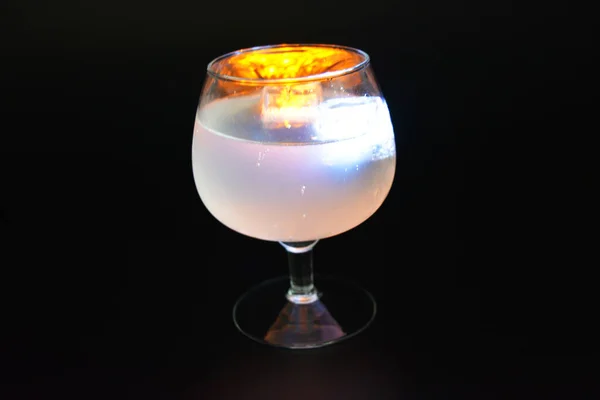 おいしい霜降り白冷たい飲み物に浮かぶ白と黄色の明るい輝く氷のキューブは 黒霜降りの背景にコニャックガラスに位置しています — ストック写真