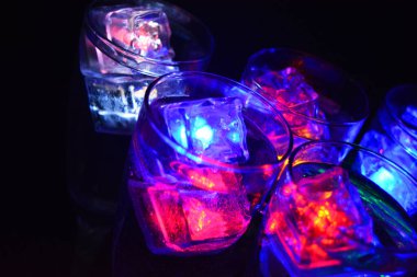 Farklı renklerde parlayan buz küpleri olan uzun burkulmuş bacaklarda beş cam kadeh. Aydınlık elementlere sahip eğlenceli ve parlak içecekler siyah bir arka plan, parti ve rahatlama üzerinde yer alır..