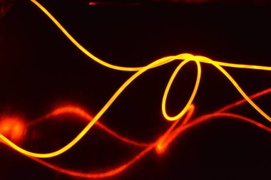 Bir ışık rehberi, turuncu ışıklı bir kablo, farklı ışık iletimli bir ışık kılavuzu, ışık tayfı ve ışık efektleri, siyah parlak arka planda ışık yansıması olan kaotik bir durumda..