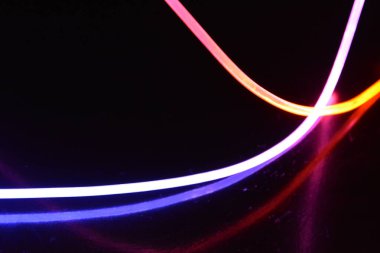 Turuncu ve mavi ışıklı bir kablo, farklı ışık iletimi, ışık spektrumuna sahip bir ışık kılavuzu kablosu, ve siyah parlak arka plan üzerinde ışık yansıması olan kaotik bir durumda bulunan ışık efektleri..