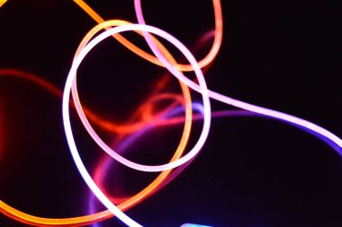 Turuncu ve mavi ışıklı bir kablo, farklı ışık iletimi, ışık spektrumuna sahip bir ışık kılavuzu kablosu, ve siyah parlak arka plan üzerinde ışık yansıması olan kaotik bir durumda bulunan ışık efektleri..