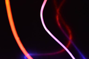 Turuncu ve mavi ışıklı bir kablo, farklı ışık iletimi, ışık spektrumuna sahip bir ışık kılavuzu kablosu, ve siyah parlak arka plan üzerinde ışık yansıması olan kaotik bir durumda bulunan ışık efektleri..