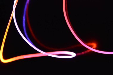 Turuncu ve mavi ışıklı bir kablo, farklı ışık iletimi, ışık spektrumuna sahip bir ışık kılavuzu kablosu, ve siyah parlak arka plan üzerinde ışık yansıması olan kaotik bir durumda bulunan ışık efektleri..