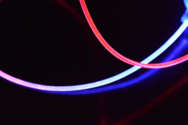 Kırmızı ve mavi ışık teli, farklı ışık iletimi, ışık spektrumu ve ışık efektleri ile siyah parlak arka planda ışık yansıması olan kaotik bir durumda..