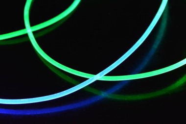 Yeşil ve mavi ışık teli, farklı ışık iletimi, ışık spektrumu ve ışık efektleri ile siyah parlak arka planda ışık yansıması olan kaotik bir durumda..