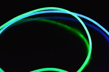 Yeşil ve mavi ışık teli, farklı ışık iletimi, ışık spektrumu ve ışık efektleri ile siyah parlak arka planda ışık yansıması olan kaotik bir durumda..