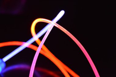 Turuncu ve mavi ışık teli, farklı ışık iletimi, ışık spektrumu ve ışık efektleri ile siyah parlak arka planda ışık yansıması olan kaotik bir durumda..