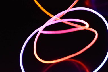 Turuncu ve mavi ışık teli, farklı ışık iletimi, ışık spektrumu ve ışık efektleri ile siyah parlak arka planda ışık yansıması olan kaotik bir durumda..