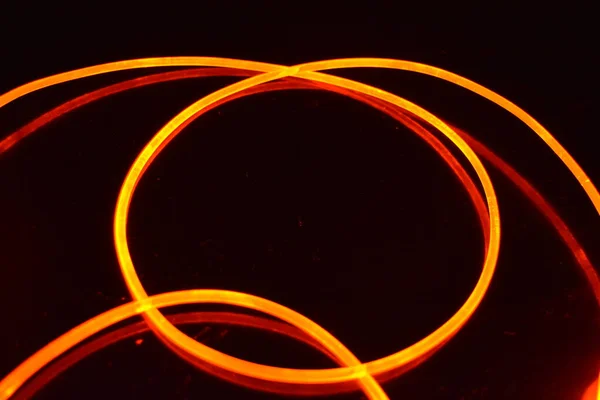 A light guide, a wire with orange light, a light guide wire with different light transmission, light spectrum, and light effects located in a chaotic state with light reflection on a black glossy background.