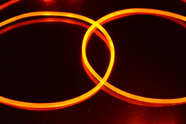 A light guide, a wire with orange light, a light guide wire with different light transmission, light spectrum, and light effects located in a chaotic state with light reflection on a black glossy background.