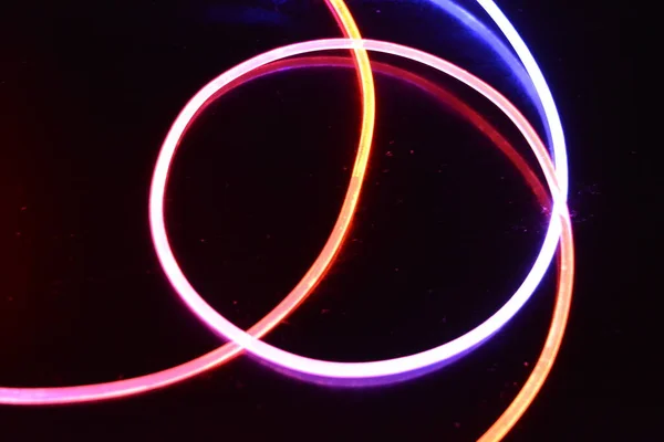 A wire with orange and blue light, a light guide wire with different light transmission, light spectrum, and light effects located in a chaotic state with light reflection on a black glossy background.