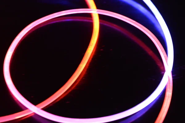 A wire with orange and blue light, a light guide wire with different light transmission, light spectrum, and light effects located in a chaotic state with light reflection on a black glossy background.