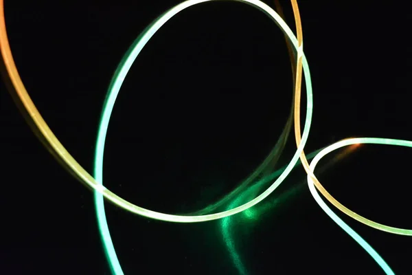 A wire with orange and green light, a light guide wire with different light transmission, light spectrum, and light effects located in a chaotic state with light reflection on a black glossy background.