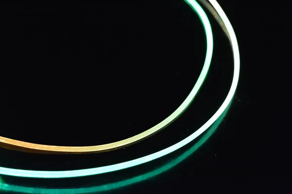 A wire with orange and green light, a light guide wire with different light transmission, light spectrum, and light effects located in a chaotic state with light reflection on a black glossy background.