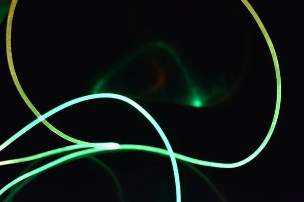 Wire with green and red light, a light guide wire with different light transmission, light spectrum, and light effects located in a chaotic state with light reflection on a black glossy background.