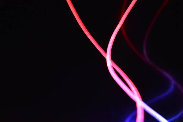 Red and blue light wire, a light guide wire with different light transmission, light spectrum, and light effects located in a chaotic state with light reflection on a black glossy background.