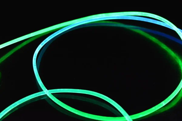 Green and blue light wire, a light guide wire with different light transmission, light spectrum, and light effects located in a chaotic state with light reflection on a black glossy background.