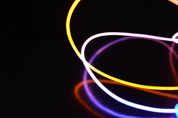 Yellow and blue light wire, a light guide wire with different light transmission, light spectrum, and light effects located in a chaotic state with light reflection on a black glossy background.