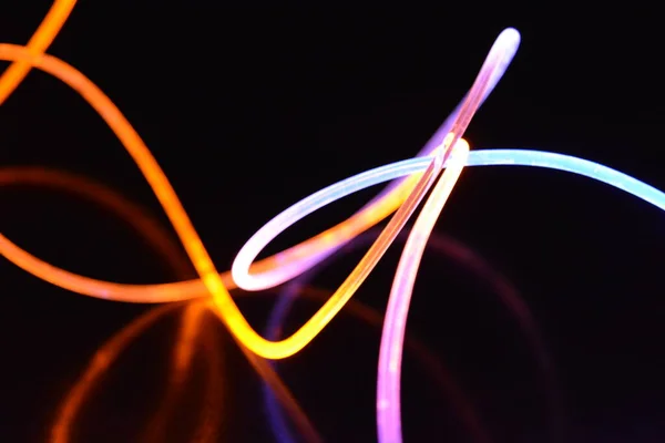 Yellow and blue light wire, a light guide wire with different light transmission, light spectrum, and light effects located in a chaotic state with light reflection on a black glossy background.