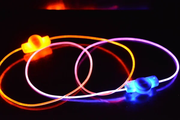 Orange and blue light wire, a light guide wire with different light transmission, light spectrum, and light effects located in a chaotic state with light reflection on a black glossy background.