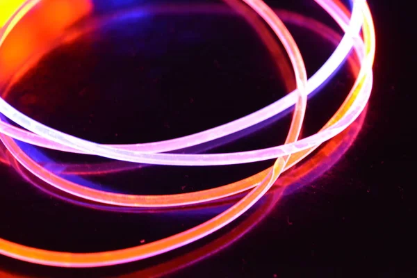 Orange and blue light wire, a light guide wire with different light transmission, light spectrum, and light effects located in a chaotic state with light reflection on a black glossy background.
