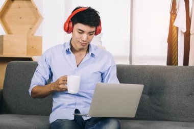Genç Asyalı adam kahve içerken ve müzik dinlerken dizüstü bilgisayarda çalışıyor..