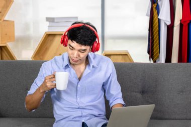 Genç Asyalı adam kahve içerken ve müzik dinlerken dizüstü bilgisayarda çalışıyor..