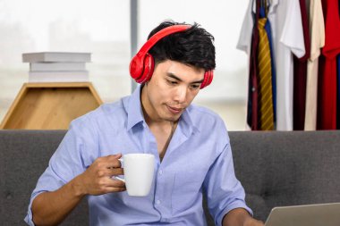 Genç Asyalı adam kahve içerken ve müzik dinlerken dizüstü bilgisayarda çalışıyor..
