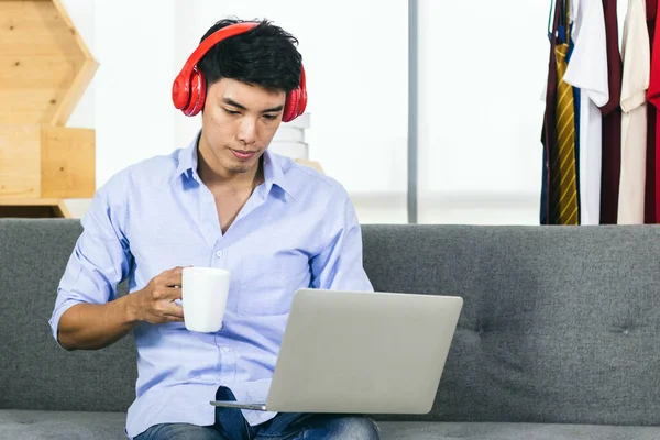 Genç Asyalı adam kahve içerken ve müzik dinlerken dizüstü bilgisayarda çalışıyor..