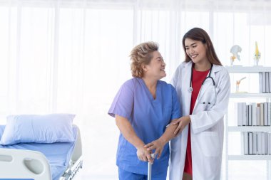 Genç ve çekici Asyalı doktor yaşlı bir hastanın yürümesine, hastaneye ve sağlık hizmetlerine yardım ediyor..
