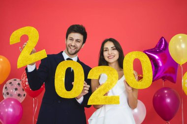 Genç çift yeni yılı birlikte kutluyor, ellerinde kırmızı arkaplanlı 2020 adet simli mektup var..